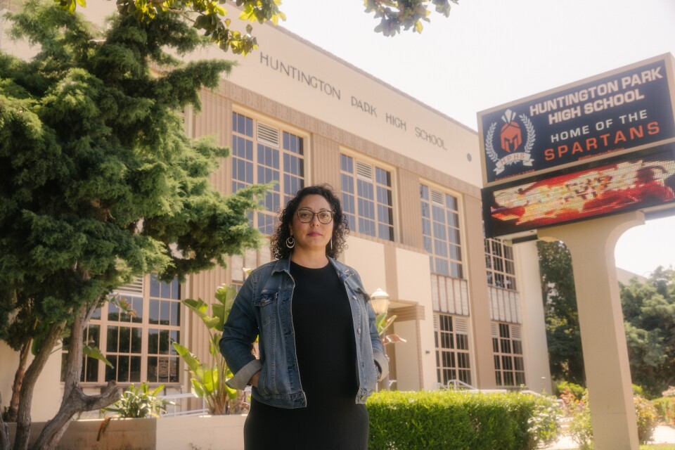 A Latina with light-tone skin stands in front of Huntington Park High.