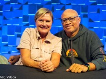 Denise Crosby, a white woman and Larry Wilmore, a Black man, smiling at the camera