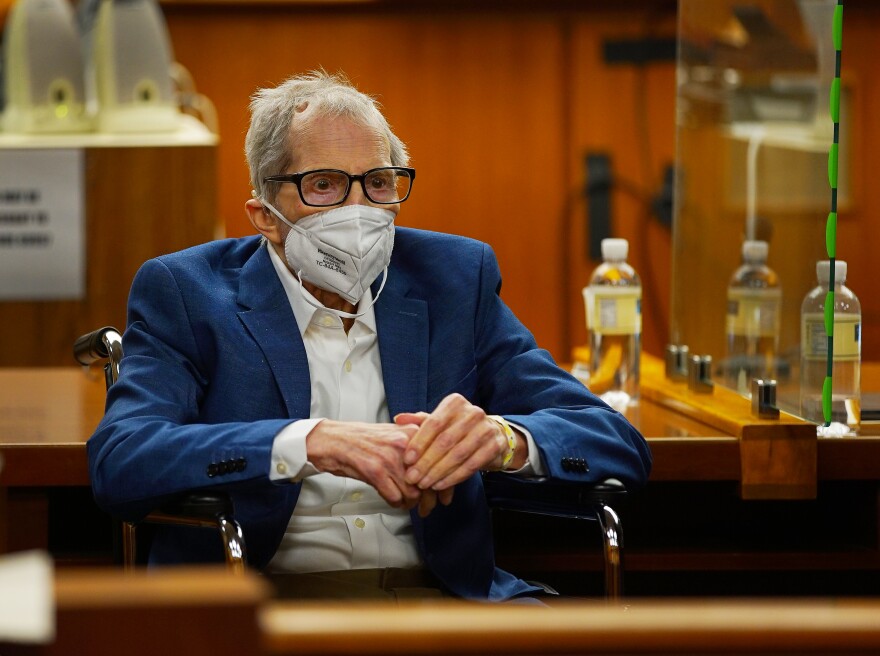 A photo of Robert Durst in the courtroom, wearing a mask and a blue suit, sitting in a wheelchair.