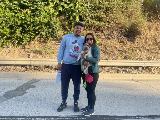 Two people posing on a freeway, holding a water bottle and a small dog.