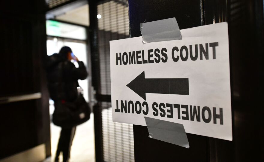 A print-out that says HOMELESS COUNT with a large arrow pointing toward a door where a person is standing, back to the camera, is taped to a window.