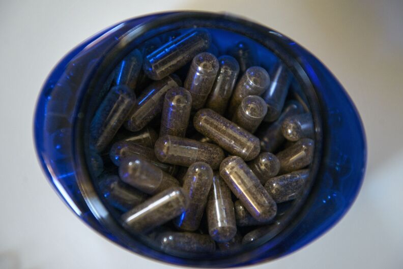 A translucent blue pill bottle filled with clear capsules containing a brown colored powder containing ground human placenta.