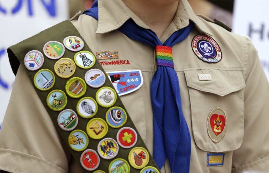 A close up of a youth wearing a khaki shirt with patches, blue tie, and a sash with patches on it.