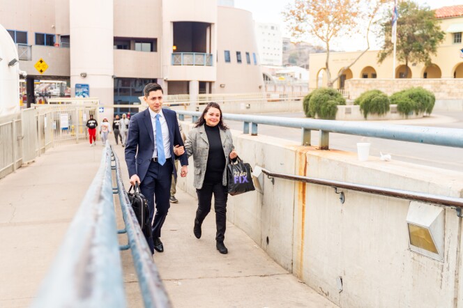 A young man in a suit and a middle-aged woman in a blazer walk up a ramp, both wearing expressions of tearful joy. 