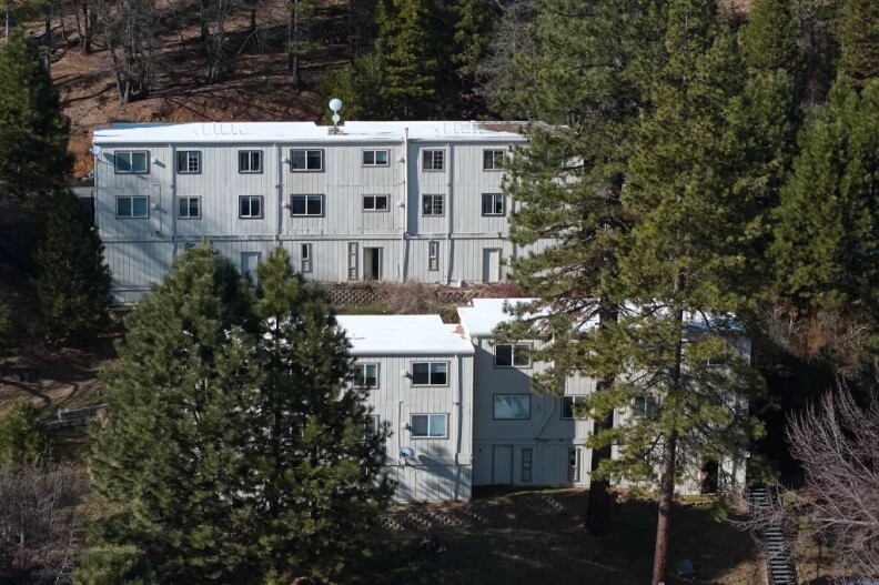 An aerial view of two white apartment buildings nestled amongst trees