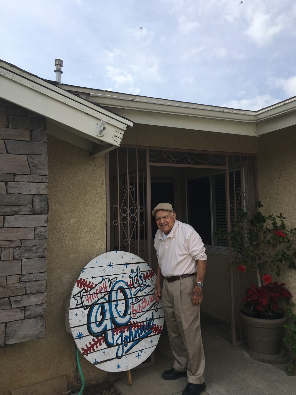 An old man stands in front of a house