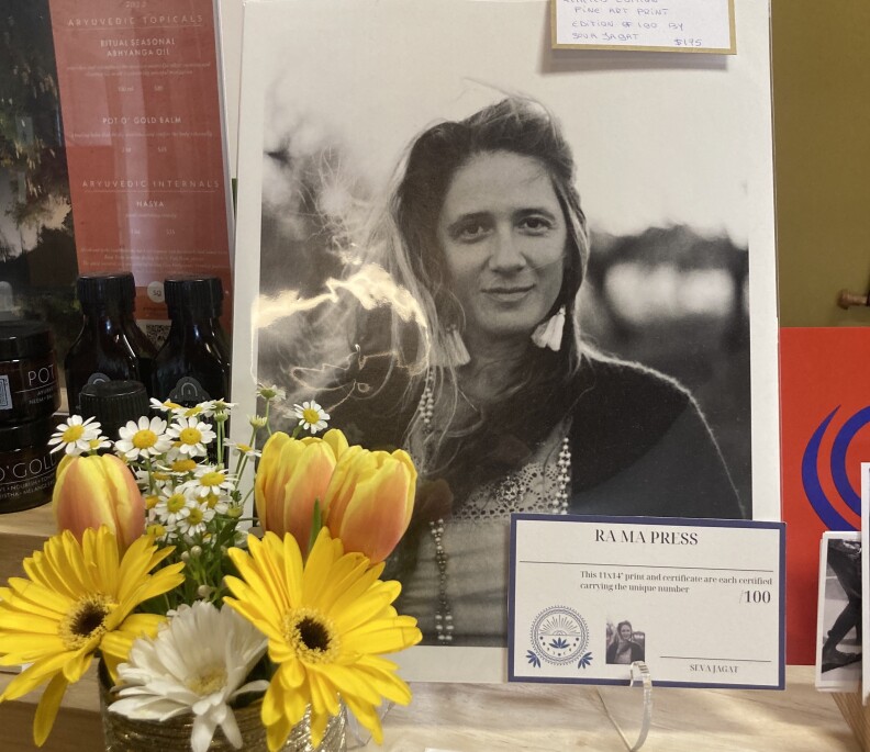 A black and white photo of a light-skinned woman slightly smiling sits on an easel with yellow flowers nearby.