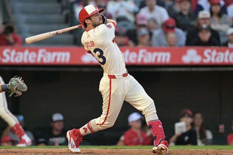 A baseball player in a white and red uniform swings a bat.