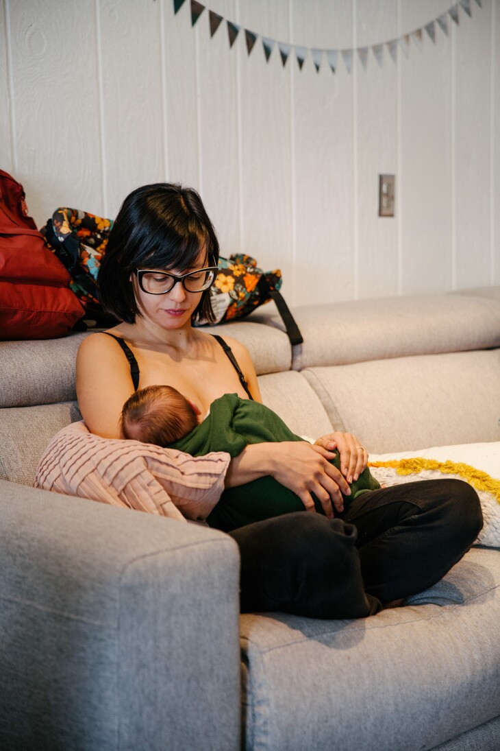 A woman with short dark brown hair and glasses holds an infant to her chest.