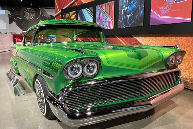 A bright-green 1950s-era classic car; in the backdrop are colorful art pieces on an earth-toned wall.