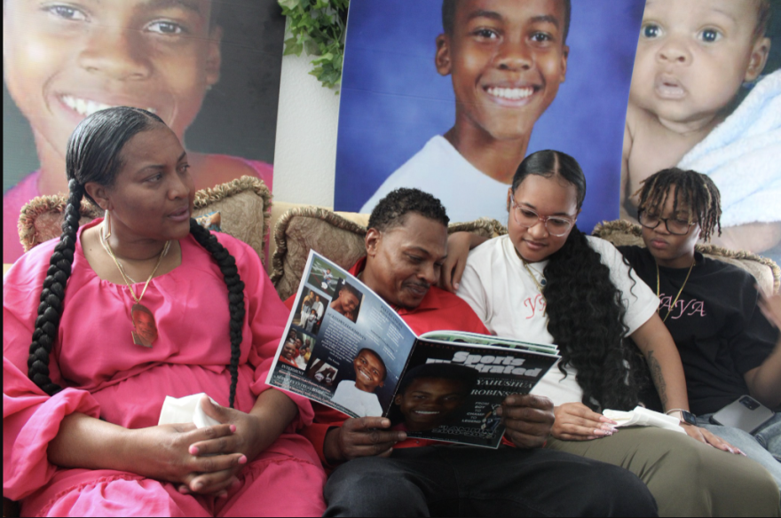 A woman, man and two children, all with brown skin tone, sit on a couch and smile while looking at a picture album.