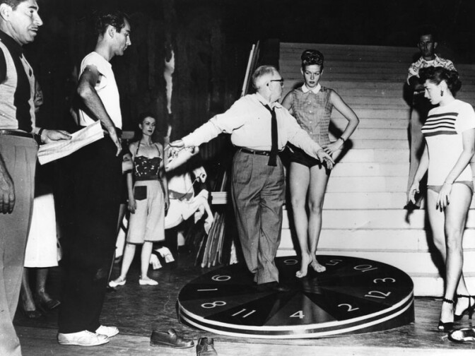 A stairway used as a prop can be seen behind cast members.