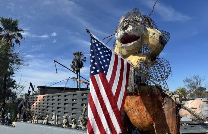 A large bunny wire topiary holding an American flag in front of a property with debris.