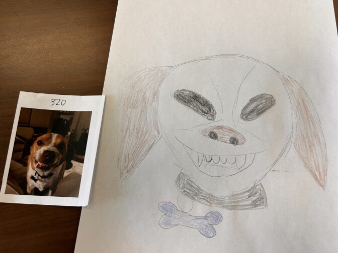 A white piece of printer paper with a hand drawn dog on it in color pencil. A small real photo of the dog is placed on the table next to it.