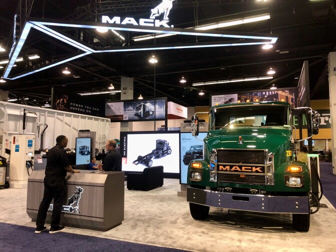 A green Mack medium-duty truck on a carpeted showfloor in a well-lit convention center. 
