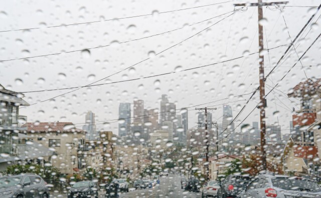 View of the downtown Los Angeles skyline from behind a rain-soaked car windshield.