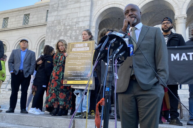 LA City Council Member Marqueece Harris-Dawson joined BLM activists and other lawmakers to call for police reforms. Harris-Dawson wears a grey suit with beige tie and holds a microphone. LA City hall can be seen in the background. 