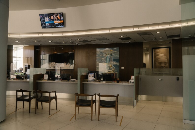 The lobby of a bank where seats are lined up in front of service counters with glass dividers.