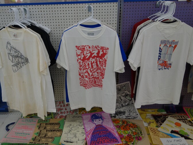 T-shirts on a rack next to store shelving, with brochures and pamphlets below.