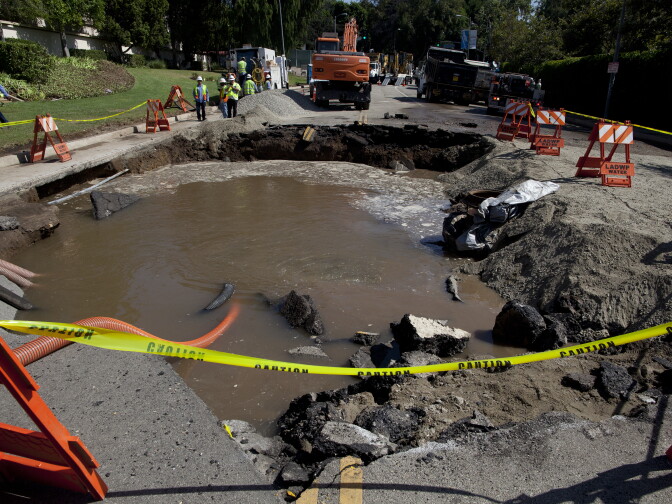 Los Angeles Department of Water and Power employees pump water out of the hole created on Sunset Boulevard after a water main ruptured and flooded parts of the UCLA campus.