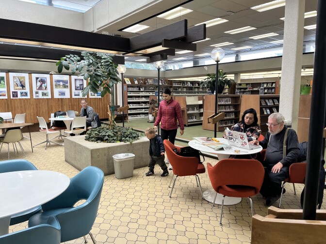 Library patrons sit at tables and walk through the atrium section of a library.