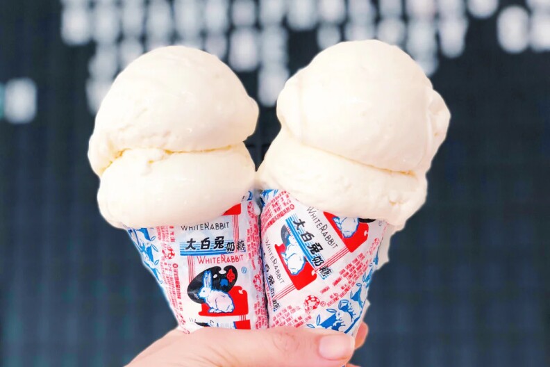 A hand holds up two ice cream cones wrapped in blue, red, and white paper.