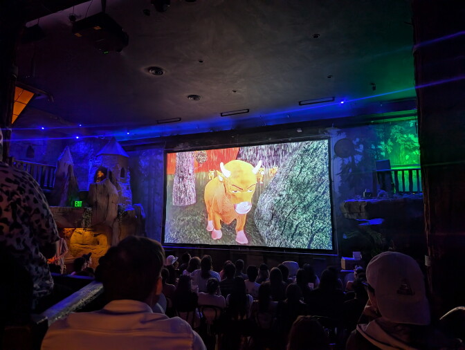 A group of people in a theater watching a film about an animated cow.