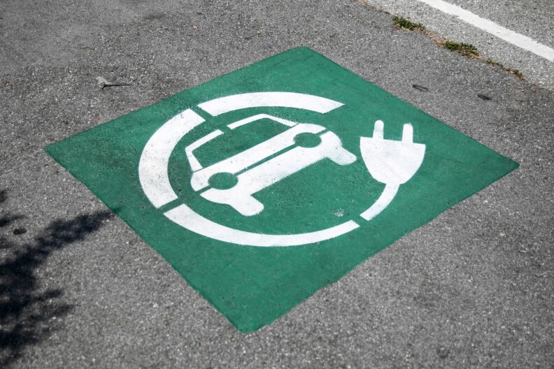 A green square is painted on a paved road. In it, there is a symbol of a car encircled by a plug, painted in white.