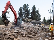 A person spraying water on a pile of rubble with a big machine moving it.