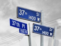A collage of blue street signs for 37th Street, 37th Place, and 37th Drive. The background is a grayed out sky and power lines.