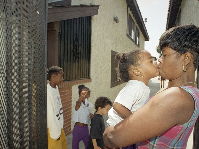 Elvira Evers holds her daughter, Jessica in front of the security gates of her apartment complex in Gardena, California, Monday, April 4, 1994 where she finally feels safe after moving from her previous residence in Compton, Calif. Evers was shot during the 1992 Los Angeles riots while pregnant with Jessica, who was born with the bullet in her elbow. In the background are son Marvin, 13, left, daughter Nella, 7, and Paris Beacon, a 5-year-old neighbor. (AP Photo/Rhonda Birndorf)