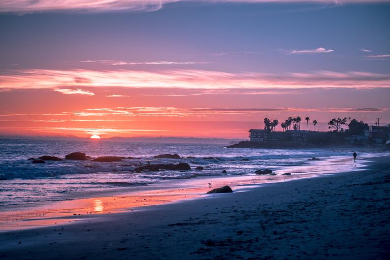 The sky is purple and orange as the sun sets over the sand and Pacific Ocean.