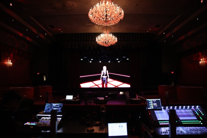 A darken room with an virtual avatar on a giant screen. 