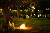 A man stands in front of a fire in a public park as other people sit on benches in the background.