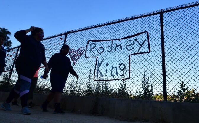 TOPSHOT - People walk past the name Rodney King seen on a chain-link fence surrounding Silver Lake Reservoir in Los Angeles, on June 9, 2020, where a new art installation protesting police brutality spells out, in colourful woven fabric, the names of unarmed African Americans who have been killed by police. - King, who was violently beaten by LAPD officers during his arrest for high speed drunk driving, became a writer after surving police brutality and died in June, 2012 from alcohol poisoning. (Photo by Frederic J. BROWN / AFP) (Photo by FREDERIC J. BROWN/AFP via Getty Images)