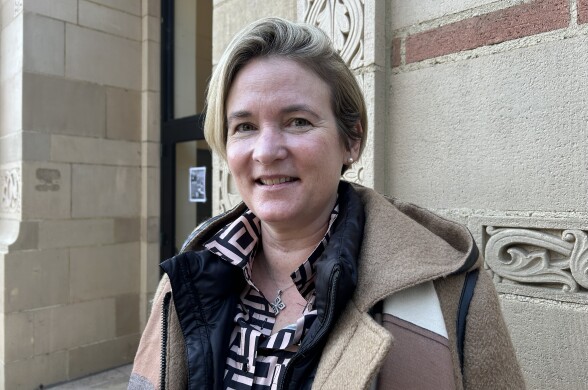 A light skinned-woman with a blonde bob smiles slightly as she poses for a portrait. She is wearing a jacket and a coat. 