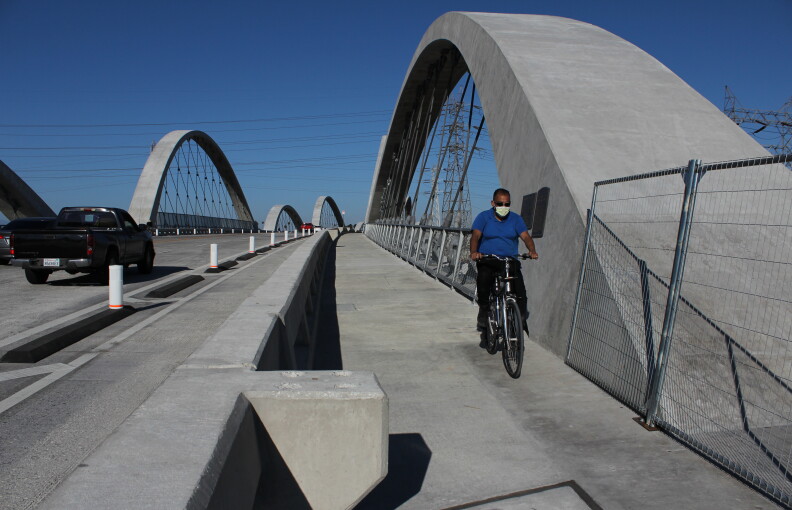 A man wearing a mask and sunglasses rides a bike along the pedestrian walkway of a new viaduct bridge.