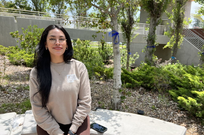 A young woman with long dark hair sits in a garden surrounded by blue ribbons.