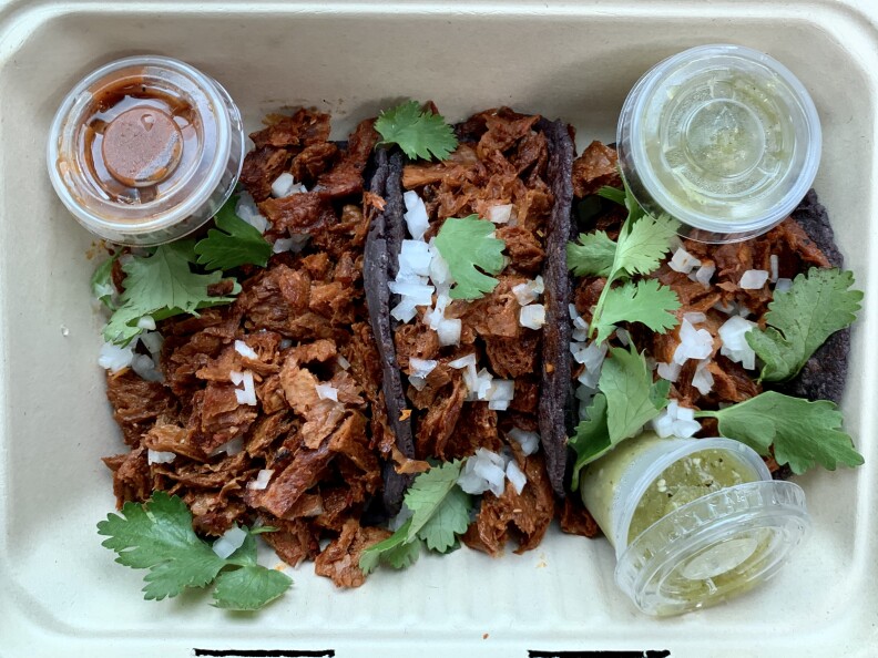 two tacos on blue corn tortillas next to a pile of plant-based meat topped with chopped onions and cilantro