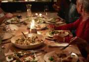 A wood table has food served family style including potatoes and salad with glasses of red and white wine. People sitting at the table have medium-skin tones.