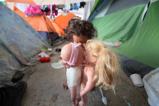 Tijuana, BAJA CALIFORNIA, Mexico - December 16, 2018.  At the El Barretal shelter in Matamoros, Tijuana, Monserrat Reyes, 3, has her new dolls kiss, as she plays near her family's tents with the toys she was given.

In Tijuana, Mexico, children members of the migrant caravan are learning to live in limbo as they move between shelters, settling in as much as possible to create a sense of normalcy, with help from NGOs, counselors and aid organizations. (Photo by Peggy Peattie)