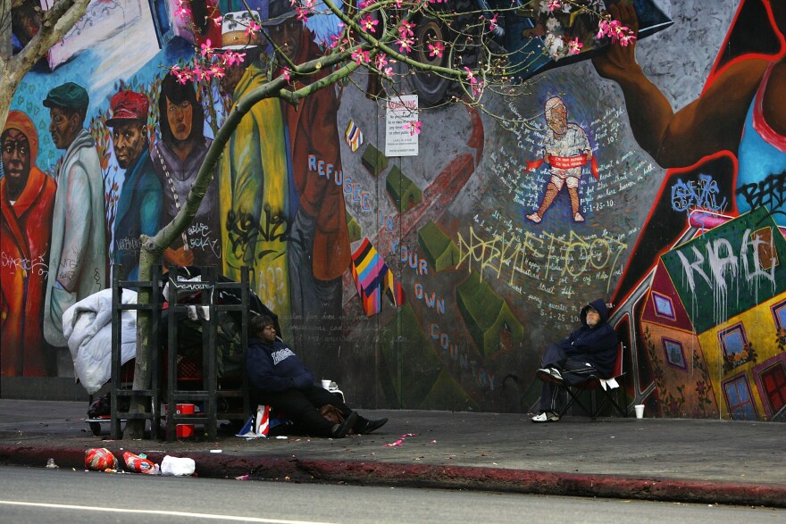 LOS ANGELES, CA - OCTOBER 12:  Homeless people sit near a mural after waking up before dawn to dismantle their beds and encampments before businesses open October 12, 2007 in the downtown Skid Row area of Los Angeles, California. Los Angeles city officials recently settled a 2003 lawsuit brought by advocates for homeless skid row residents who complained of being arrested for sleeping on sidewalks, despite having nowhere else to go. Under the new deal, people can sleep on Los Angeles sidewalks between 9 p.m. to 6 a.m. as long as they do not block doorways or driveways, or completely block the sidewalk. Los Angeles is often referred to as the homeless capital of the nation because of its estimated 40,144 people living on city streets and 73,000 homeless spread across the county, according to recent figures attributed to the Los Angeles Homeless Services Authority, The 73,000 homeless include 10,000 minors, 24,505 people suffering from a mental illness, 8,453 military veterans, and nearly 7,200 victims of domestic abuse.  (Photo by David McNew/Getty Images) 