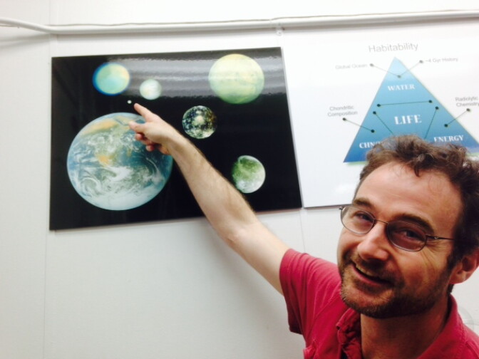 Kevin Hand shows off a poster with Earth and all the other planets and moons scientists life may exist. Hand points to Saturn's moon Enceladus which is smaller than Earth's moon.