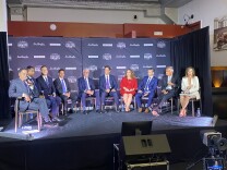 Ten people sit in chairs on a stage.
