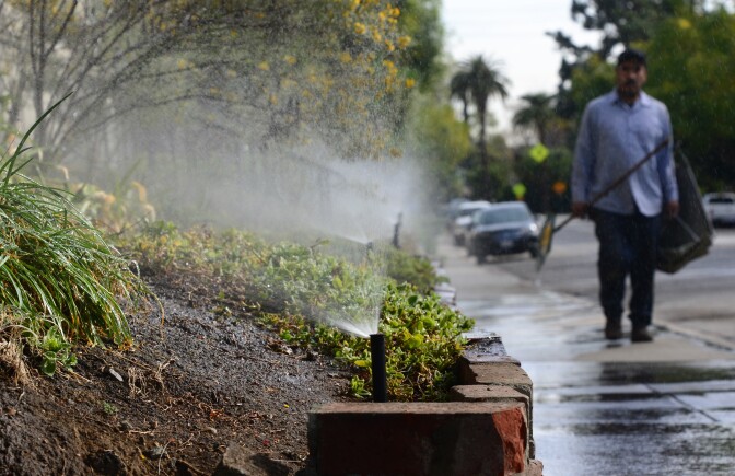 A gardener walks past a row of sprinklers watering plants and foliage in front of an apartment complex in South Pasadena, California on Jan. 21, 2014. Water is running off the plants and onto the street. This kind of wasteful use of water could soon be permanently banned in California.