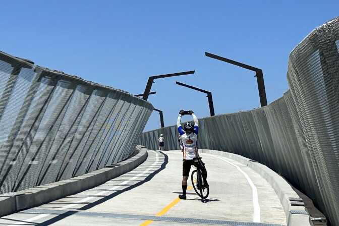 A cyclist in full gear taking a picture of the new bridge he is on.