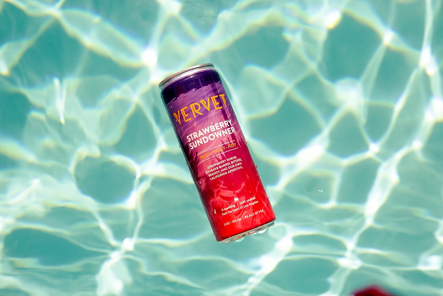 a red and pink aluminum can floats in a swimming pool