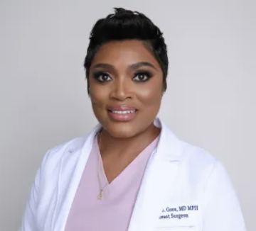 A Black doctor with short brown hair smiles as she looks at the camera.