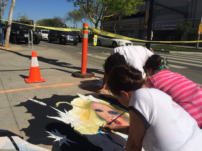 Artists from We Talk Chalk create a 3D street painting on the corner of Santa Monica Blvd and Westmount Dr in West Hollywood. The image is designed to catch people's attention before crossing the street so they aren't on their phones.