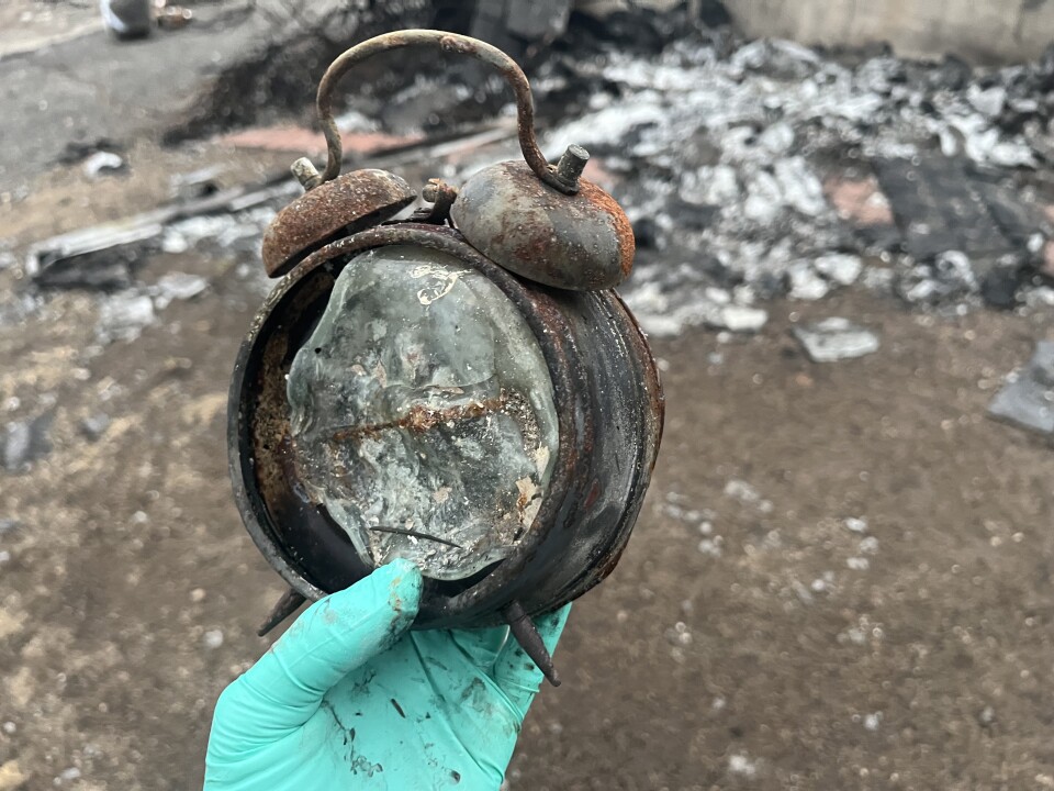 A charred alarm clock is held by a gloved hand